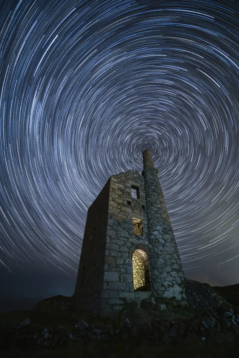 Star trails forming circles in the sky above an abandoned Cornish tin mine lit up from the inside