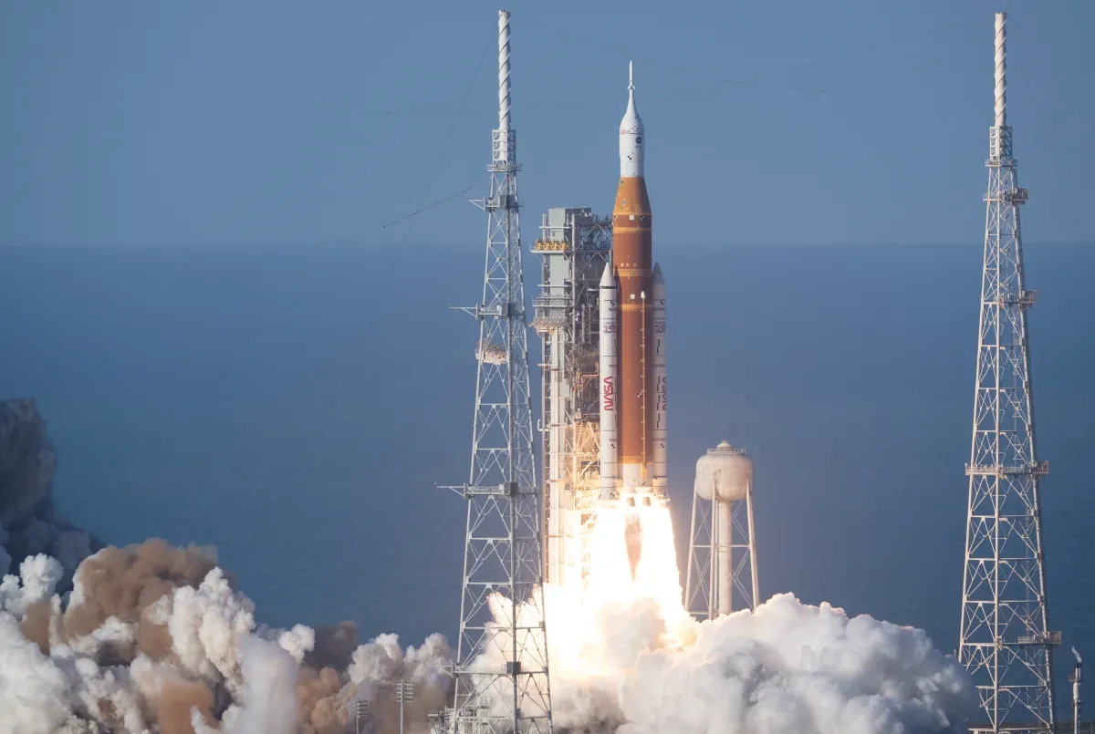 Orange Artemis 2 rocket launching just above launch pad, with huge clouds underneath
