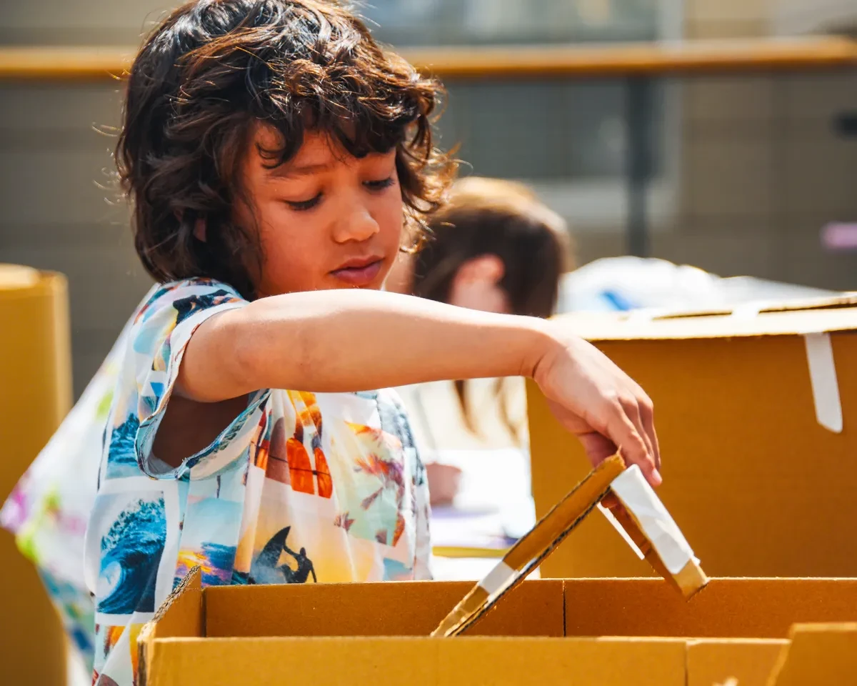 A young boy lifts the lid of a cardboard box during a craft activity at the National Maritime Museum