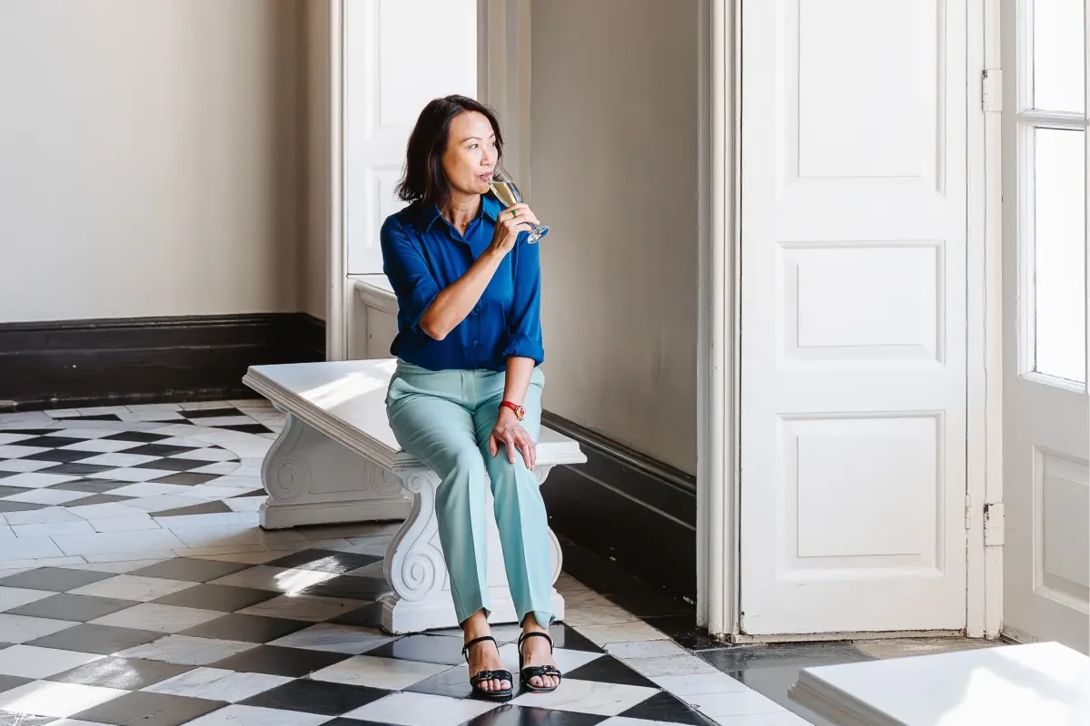 A patron wearing a blue shirt and smart light blue trousers enjoys a glass of champagne sitting in the Great Hall of the Queen's House in Greenwich