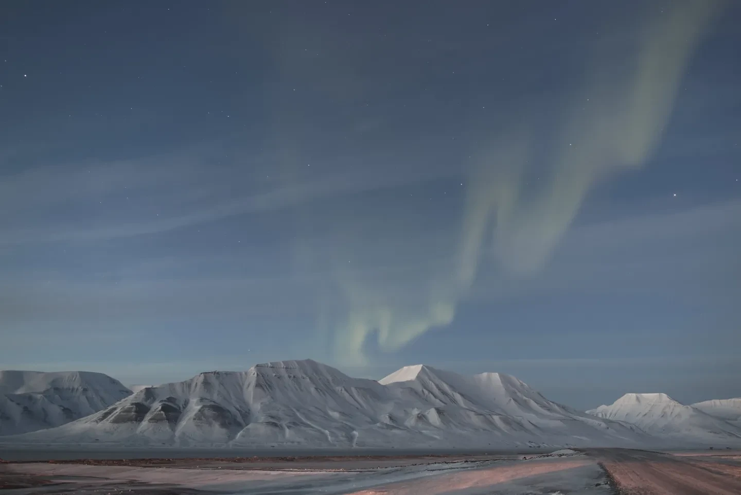 Aurora in a twilight sky above snowy mountains.