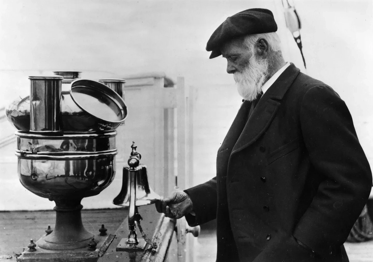 Black and white photograph of Captain Woodget inspecting ship's bell with binnacle