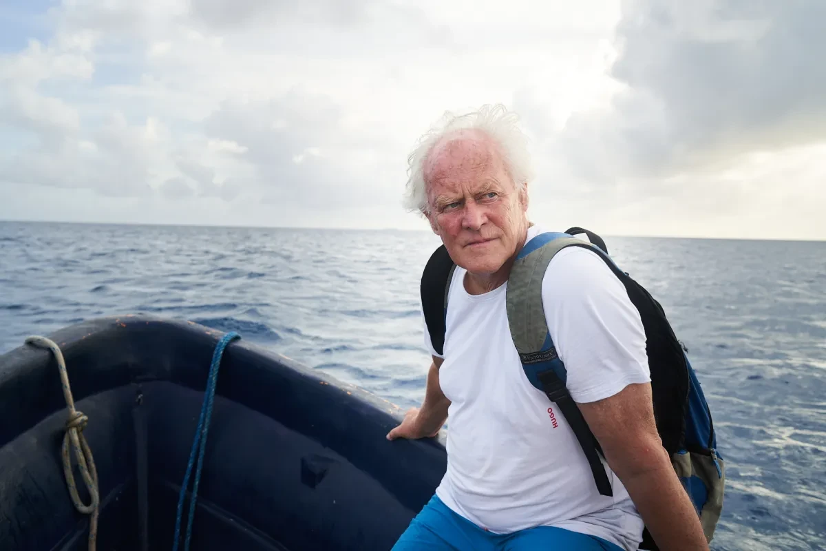 Photo of David Buckland sitting on a rock with the sea behind