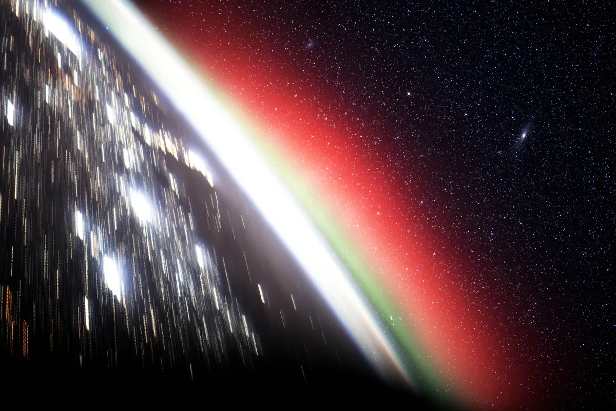 Photo taken from International Space Station looking at the Earth with silver lights on it, with green and pink aurorae on the horizon and lots of stars in space