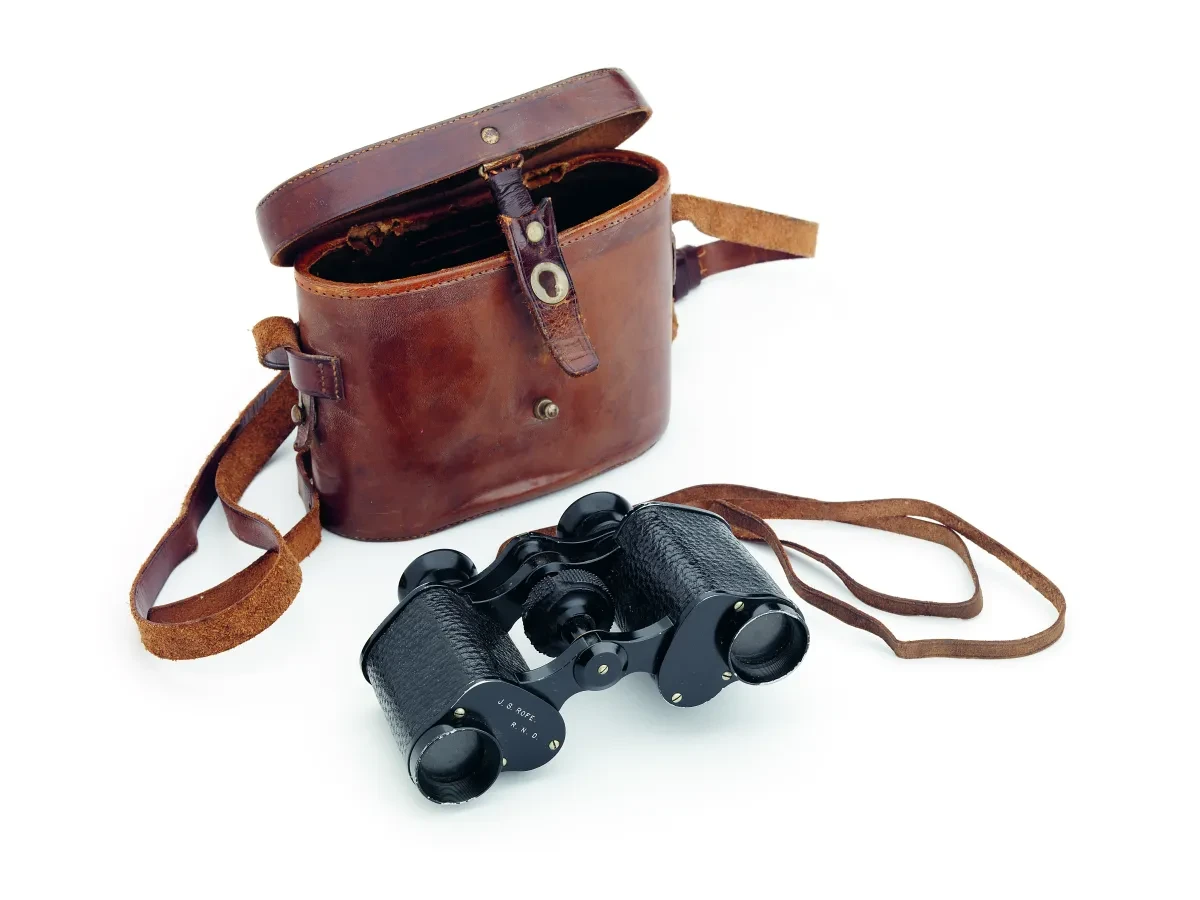 Photo of pair of black binoculars next to brown leather case