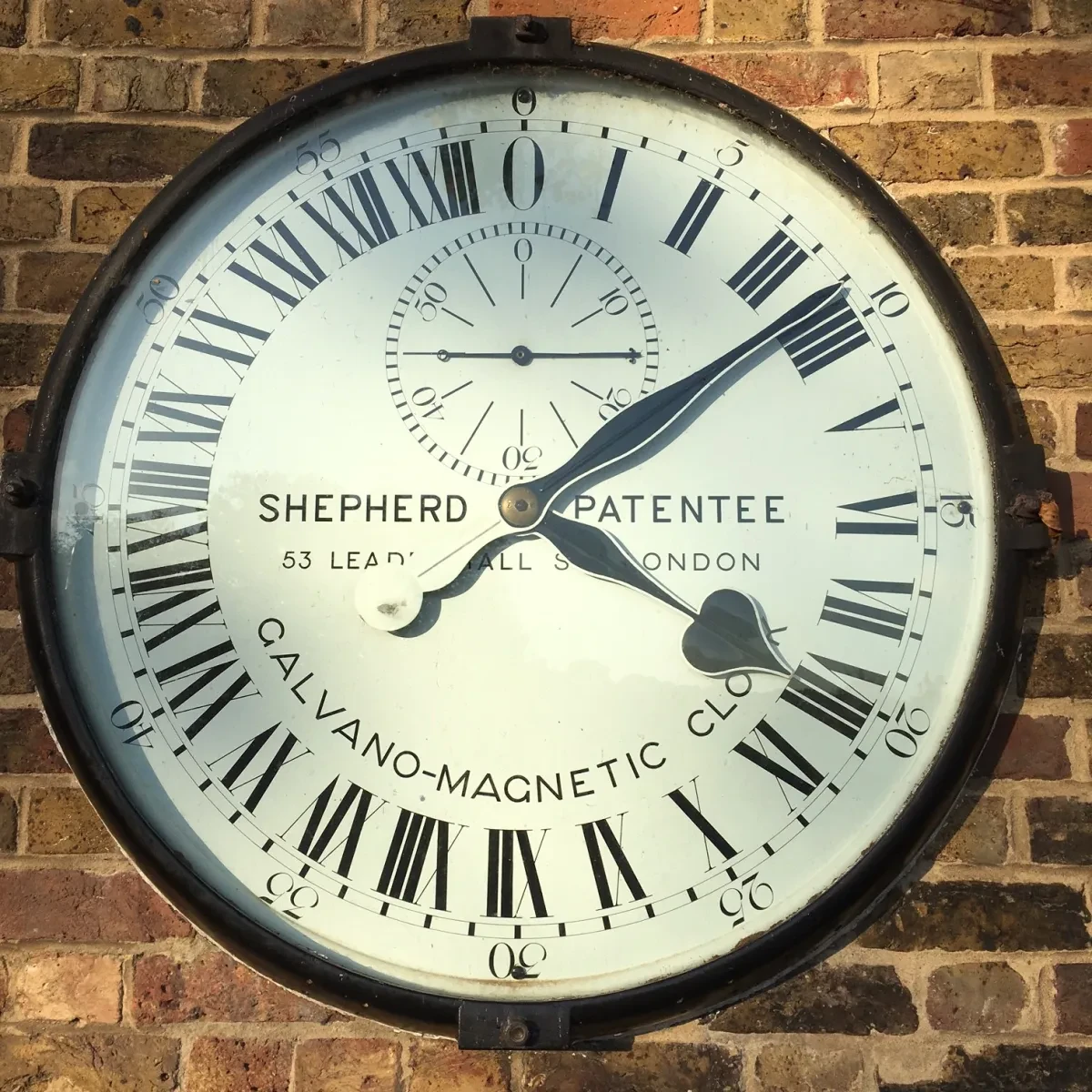 Black and white Shepherd Gate Clock on a brick wall. 