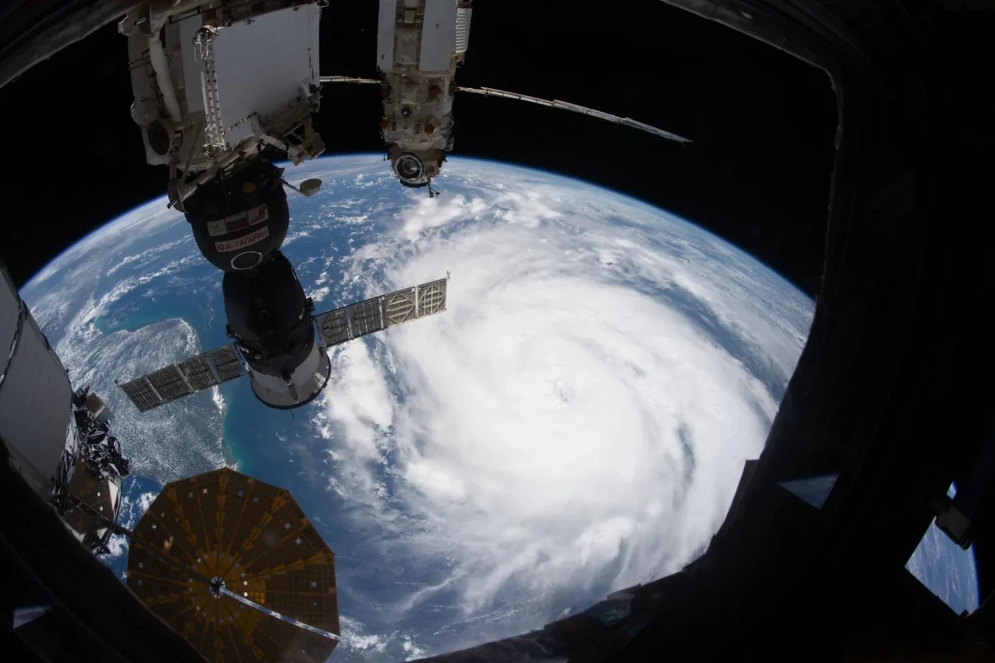 View of a hurricane from the International Space Station. The storm is a swirling mass of white cloud, with instruments on the space station visible in the foreground