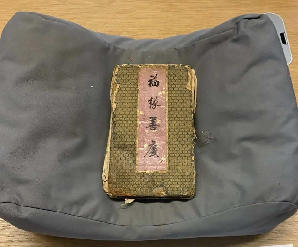 A manuscript item laying on a support pillow. There are four Chinese characters printed on the cover. 