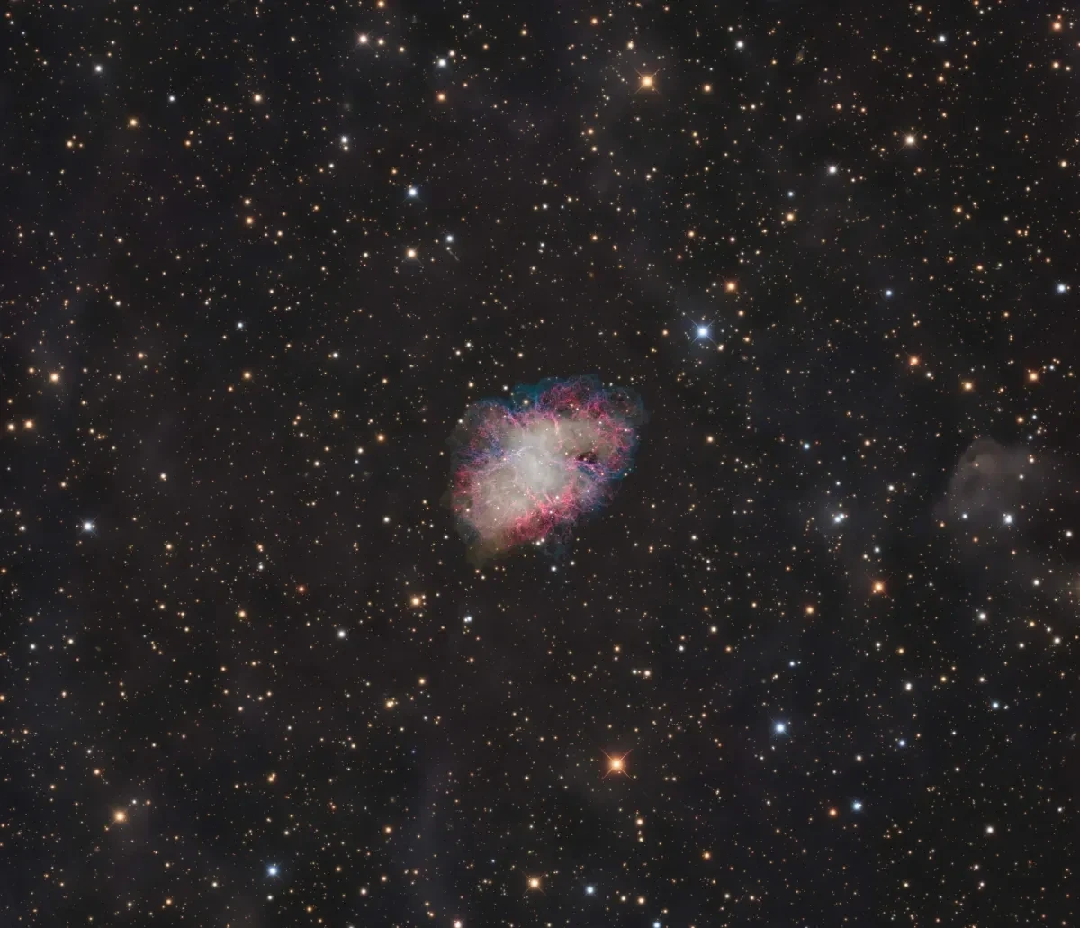 At the centre of a black, star-spotted sky, there's a glowing nebula with red, pink, purple and blue streaks