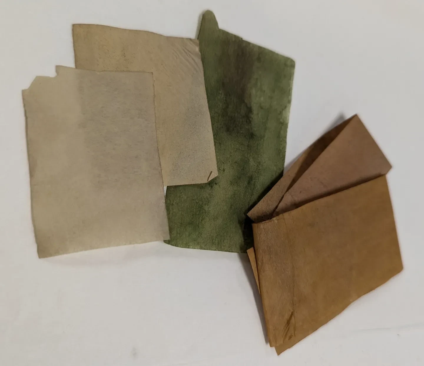 Multiple sheets of thin paper in muted cream, green and brown colours