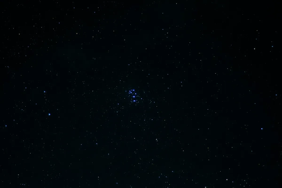 Image of dark black sky with bright cluster of blue stars in the middle
