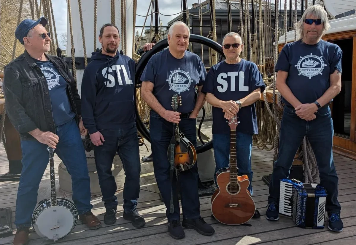 Photograph of 5 musicians on the deck at Cutty Sark with an assortment of instruments