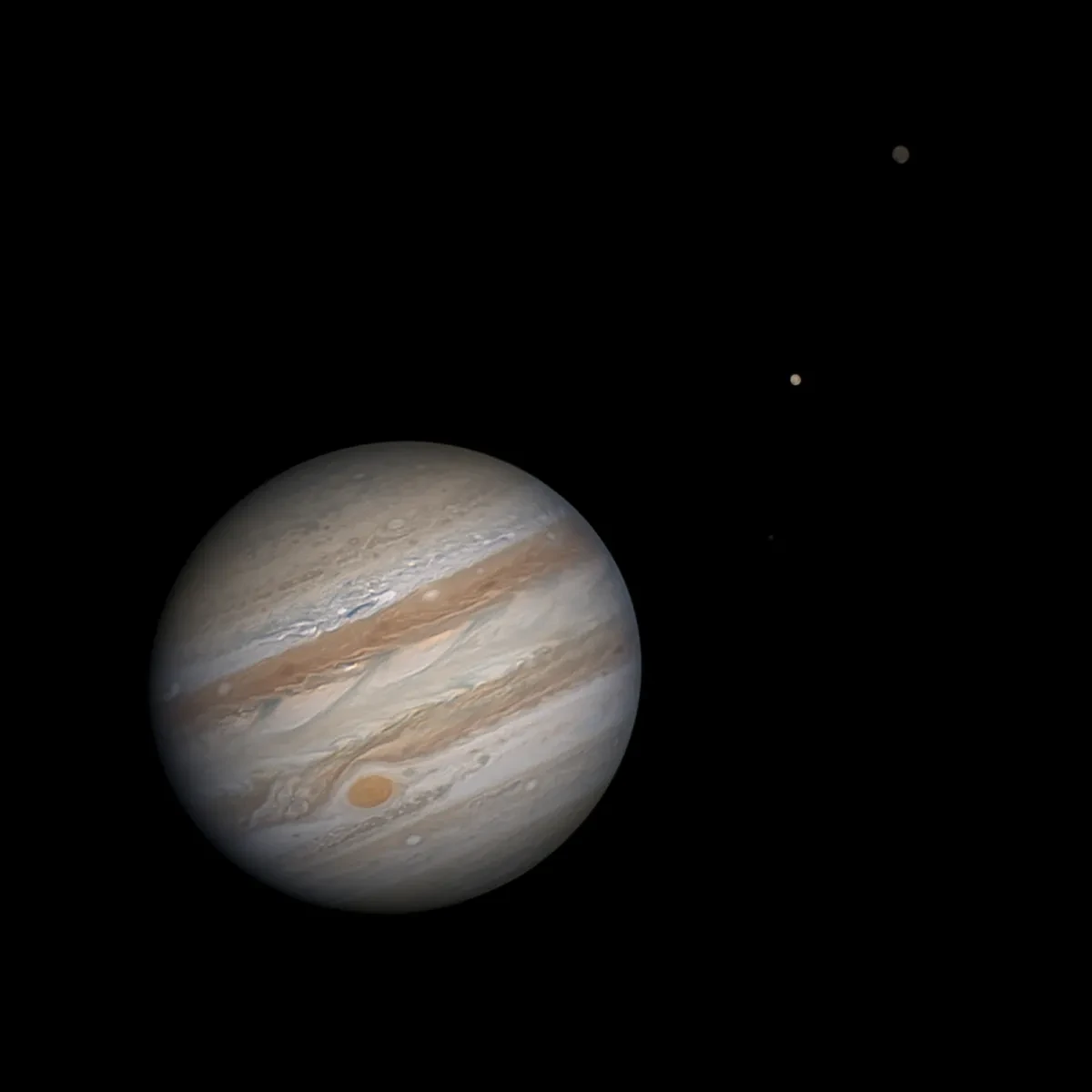 Storm-banded Jupiter and its moons in a black sky.