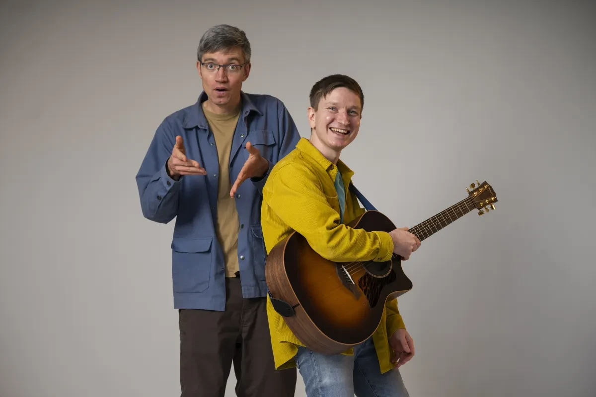 Photograph of poet Simon mole in a blue jacket and musician Gecko in a yellow shirt, holding a guitar