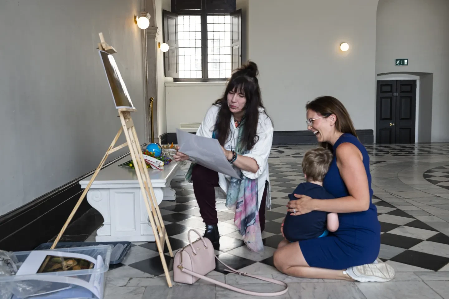 A family look at an image on an easel and laugh with a character actor. 