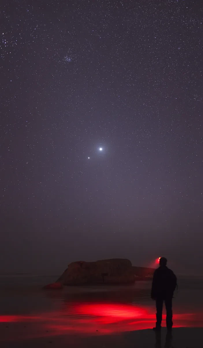 Image of man standing looking at night sky, which has two bright lights close together which are Venus and Jupiter